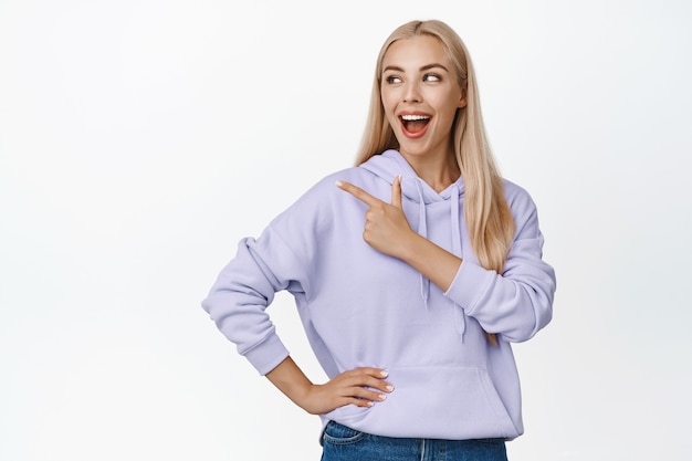 Portrait de femme heureuse naturelle riant, pointant et regardant à gauche debout sur blanc