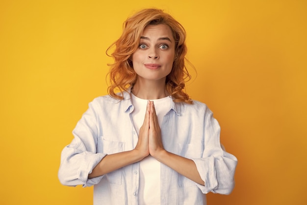 Portrait d'une femme heureuse souriant et disant la prière Jolie fille bénéficie d'une atmosphère paisible se tient la main dans un geste de prière isolé sur fond jaune