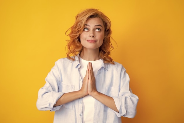 Portrait d'une femme heureuse souriant et disant la prière Jolie fille bénéficie d'une atmosphère paisible se tient la main dans un geste de prière isolé sur fond jaune