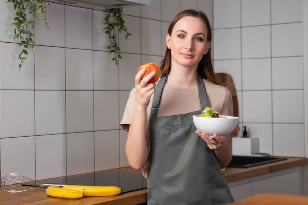 Portrait d'une femme heureuse tenant une assiette de salade fraîche et jetant une pomme fraîche vers le haut