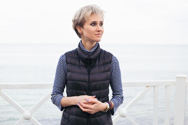 Portrait de femme hipster souriante près de la mer Modèle féminin aux cheveux courts ayant une promenade par temps nuageux Nature concept de temps libre