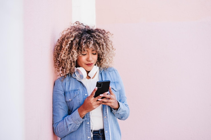 Photo portrait d'une femme hispanique souriante avec des cheveux afro en ville utilisant un téléphone portable et un casque.