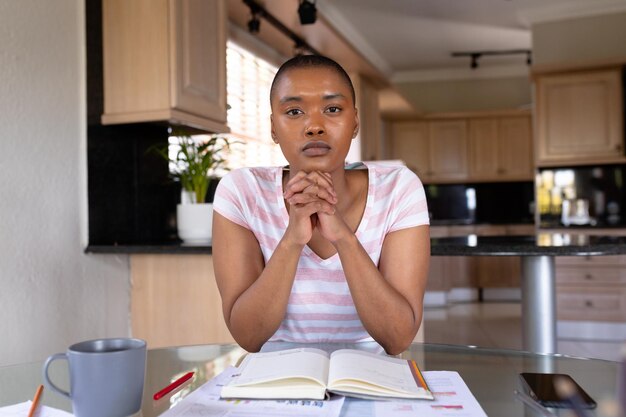 Portrait d'une femme indépendante biraciale assise avec les mains jointes au bureau à domicile. concept inchangé, de bureau à domicile, d'entreprise et d'indépendant.