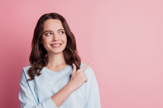 Portrait de femme indiquer le doigt montrant sur le côté du copyspace le visage joyeux sur le mur rose