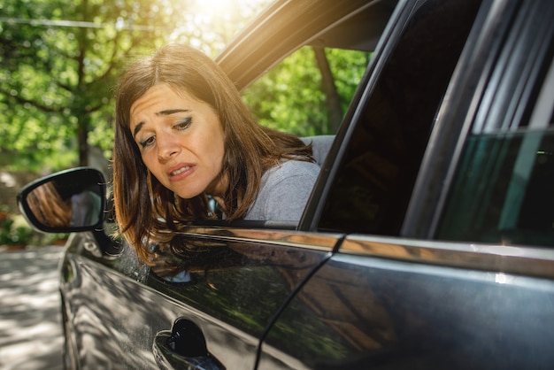Portrait de femme à l'intérieur de la voiture regardant par la fenêtre avec un visage inquiet peut-être parce que la voiture rayée pendant le stationnement ou un accident à l'arrière.