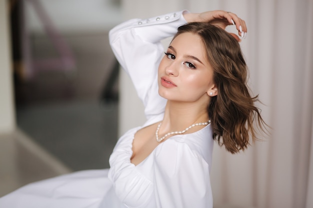 Portrait de femme jeune et élégante en robe blanche avec un beau maquillage et une coiffure magnifique