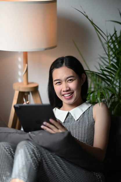 Portrait de femme joyeuse assise sur un canapé et souriant à la caméra.