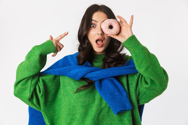 Portrait de femme joyeuse dans des vêtements décontractés tenant un beignet sucré, debout isolé sur blanc