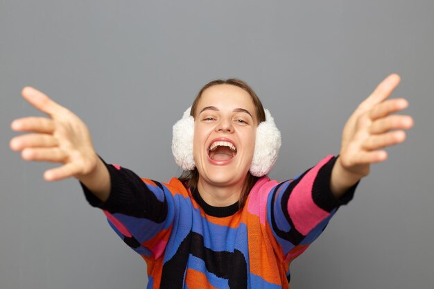 Portrait d'une femme joyeuse extrêmement heureuse portant un chandail coloré posant isolé sur fond gris écarte les bras veut embrasser quelqu'un se réjouissant d'une réunion inattendue