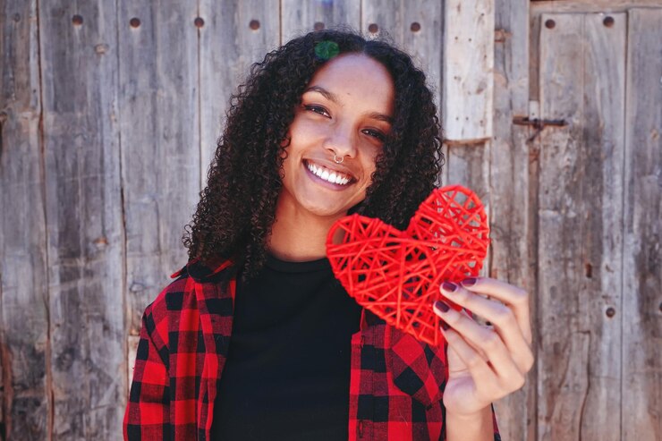 Photo portrait d'une femme joyeuse tenant une forme de cœur rouge contre un mur en bois