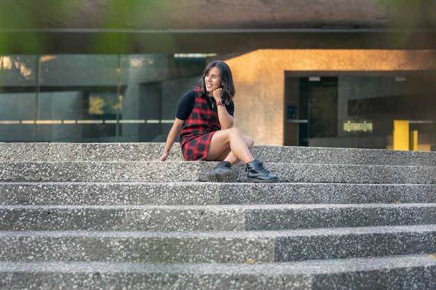 Portrait d'une femme latine gaie s'asseyant sur les escaliers d'un bâtiment avec la lumière de coucher du soleil