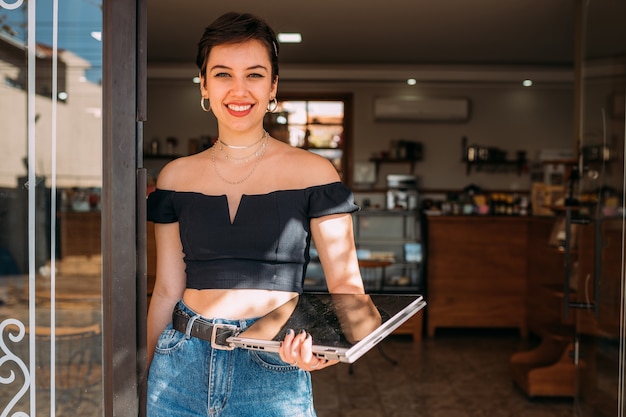 Portrait d'une femme latine heureuse debout à la porte de son magasin