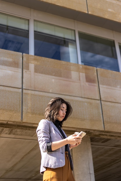 Portrait d'une femme latine en vêtements décontractés intelligents envoyant des SMS dans la rue devant son bureau