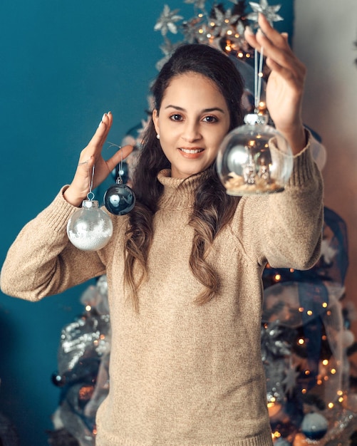 Portrait d'une femme latino-américaine tenant des boules de verre décorées avec ses mains derrière un fond de Noël