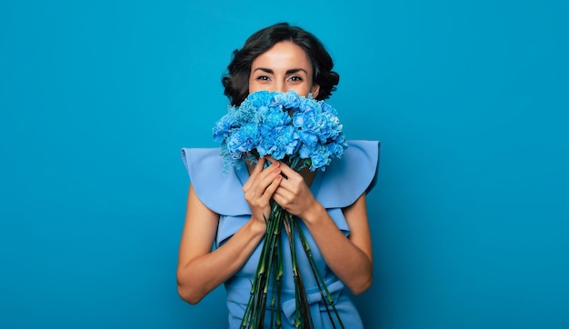 Portrait d'une femme magnifique, qui regarde dans l'appareil photo et cache une partie de son visage sur le bouquet de fleurs bleues. Fête des mères. Les vacances des femmes. Printemps. Les droits des femmes. Le 8 mars