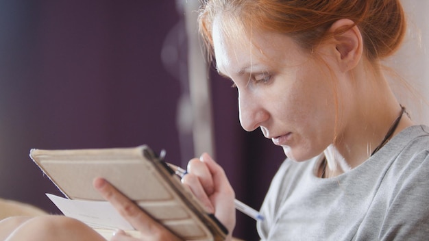 Portrait de femme à la maison assise sur un canapé et travaillant avec un gadget et un ordinateur portable, gros plan