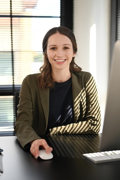 Portrait d'une femme manager caucasienne en costume élégant assise sur son lieu de travail et souriant à la caméra