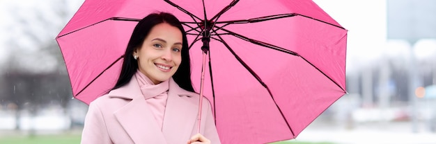 Portrait de femme en manteau qui se tient sous la pluie et détient des images élégantes de parapluie rose pour les pluies