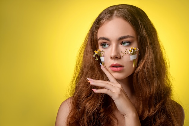 Portrait d'une femme, avec des marguerites sous les yeux, regardant sur le côté isolé sur jaune