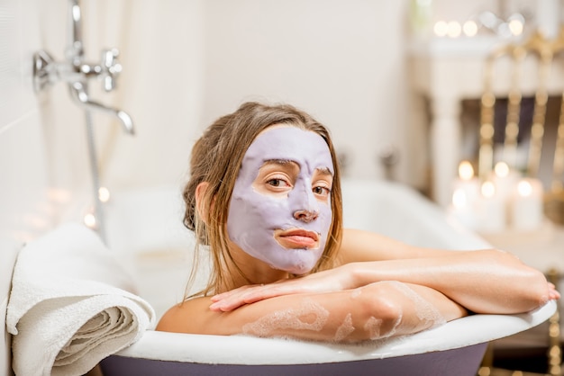 Portrait d'une femme en masque facial allongé dans la baignoire rétro de la salle de bain