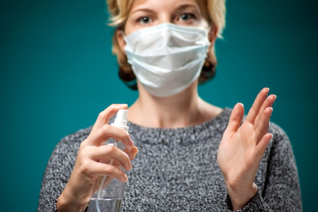 Un portrait de femme avec un masque facial médical appliquant un spray désinfectant sur les mains. Concept de personnes, de médecine et de soins de santé. Protection contre le coronavirus