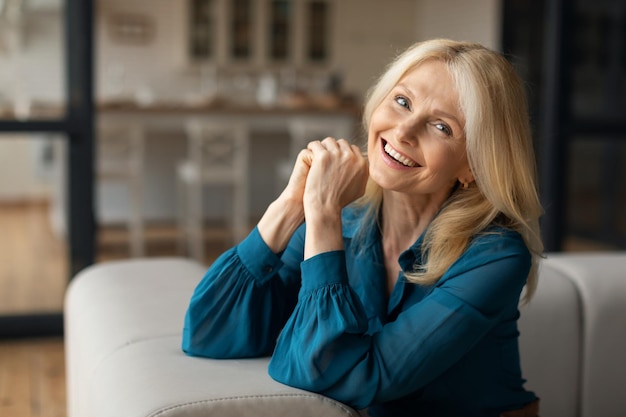 Portrait d'une femme mature caucasienne heureuse reposant sur un canapé à l'intérieur de la maison regardant et souriant à