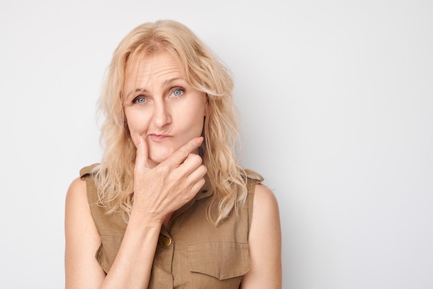 Portrait d'une femme mature intelligente touchant le menton pensant choisit des doutes isolés sur un fond de studio blanc avec un espace de copie