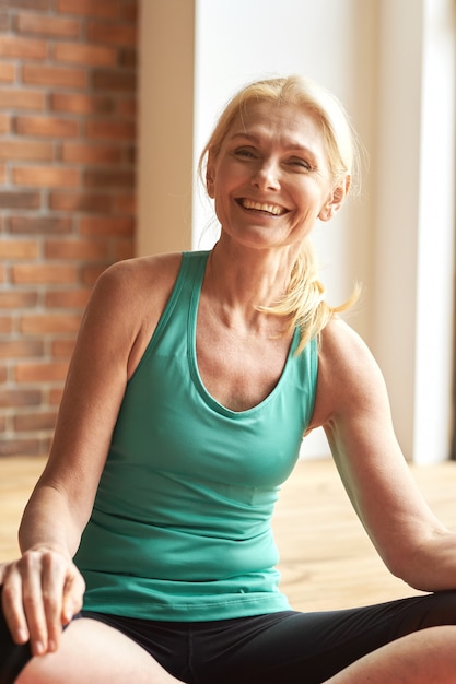 Portrait d'une femme mature sportive joyeuse souriante à la caméra assise sur le sol après une intensification