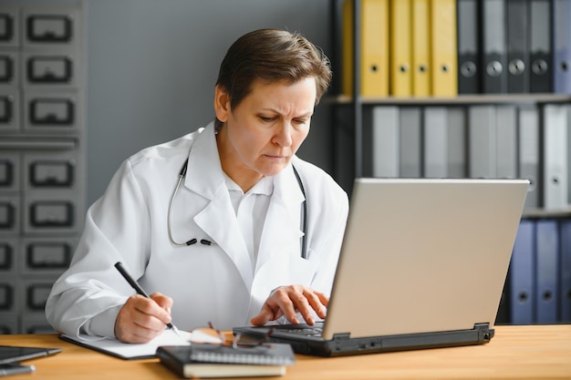 Portrait d'une femme médecin d'âge moyen assise au bureau et travaillant au bureau