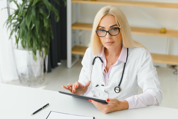 Portrait d'une femme médecin d'âge moyen assise au bureau et travaillant dans un cabinet médical