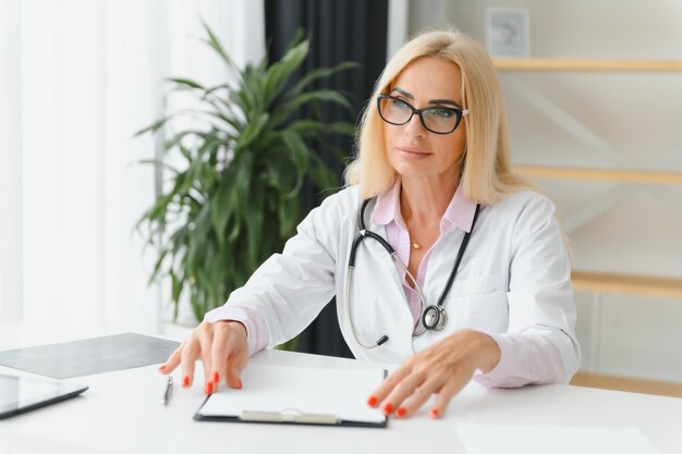 Portrait d'une femme médecin d'âge moyen assise au bureau et travaillant dans un cabinet médical