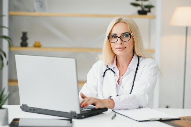 Portrait d'une femme médecin d'âge moyen assise au bureau et travaillant dans un cabinet médical