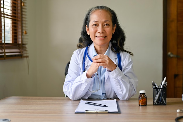 Portrait d'une femme médecin asiatique asiatique en robe blanche assise à son bureau