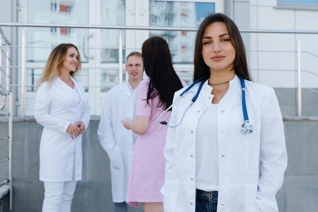 Portrait d'une femme médecin en blouse blanche à l'extérieur de la clinique Des collègues se tiennent à l'arrière-plan et parlent