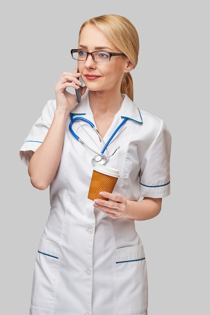 Portrait d'une femme médecin tenant une tasse de café en papier et parler au téléphone