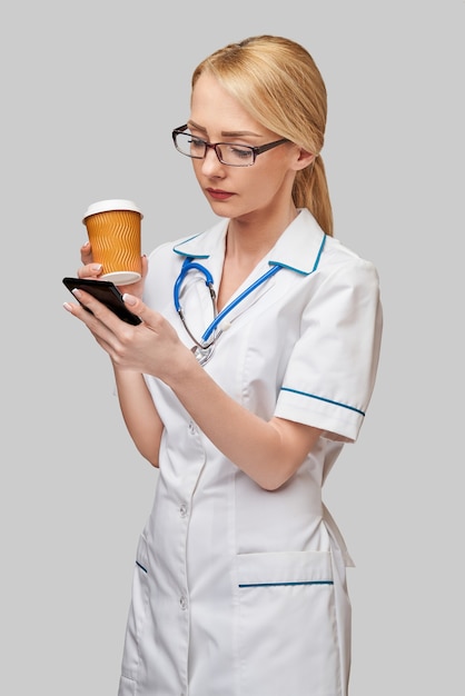 Portrait d'une femme médecin tenant une tasse de café en papier et parler au téléphone