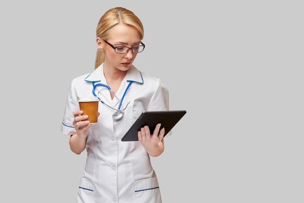 Portrait d'une femme médecin tenant une tasse de café en papier et tenant un pad tablet pc