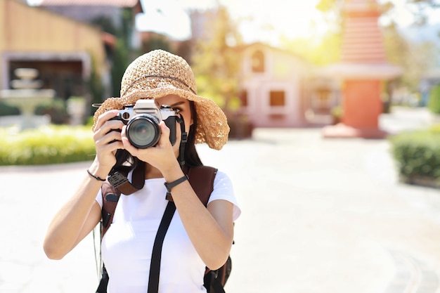 Portrait femme mignonne photographe asiatique couvrir son visage avec un appareil photo. Attrayant beau voyageur femmes asiatiques en chemise blanche et chapeau avec sac à dos s'amuser dans l'heure d'été en plein air de la ville d'Asie.