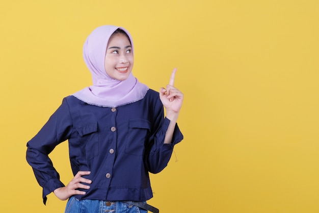 Portrait de femme mignonne pointant vers le haut en tissu décontracté portant le hijab sur fond jaune isolé