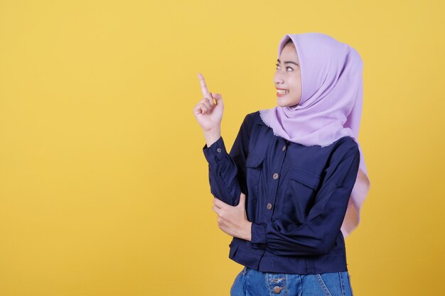 Portrait de femme mignonne pointant vers le haut en tissu décontracté portant le hijab sur fond jaune isolé