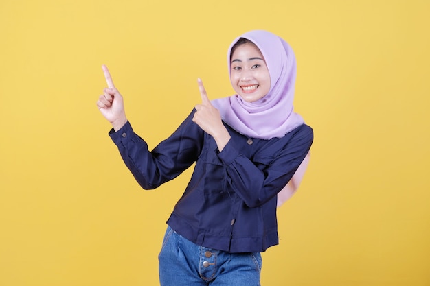 Portrait de femme mignonne pointant vers le haut en tissu décontracté portant le hijab sur fond jaune isolé