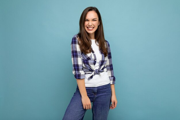 Portrait de femme à la mode gaie positive en tenue hipster isolée sur fond bleu avec