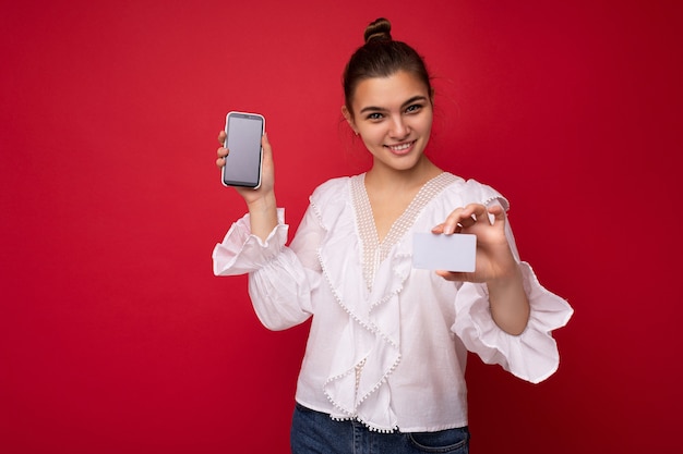 Portrait d'une femme à la mode gaie et positive en tenue de soirée tenant et montrant un téléphone portable avec