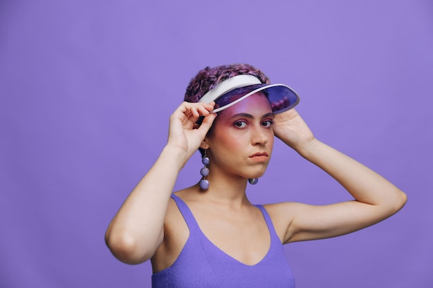 Portrait d'une femme de mode sportive posant dans un costume de sport violet pour le yoga et une casquette transparente sur fond violet monochrome