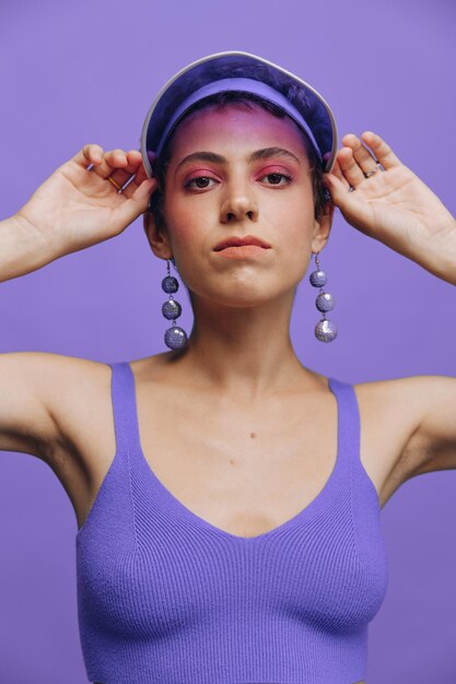 Portrait d'une femme de mode sportive posant dans un costume de sport violet pour le yoga et une casquette transparente sur fond violet monochrome