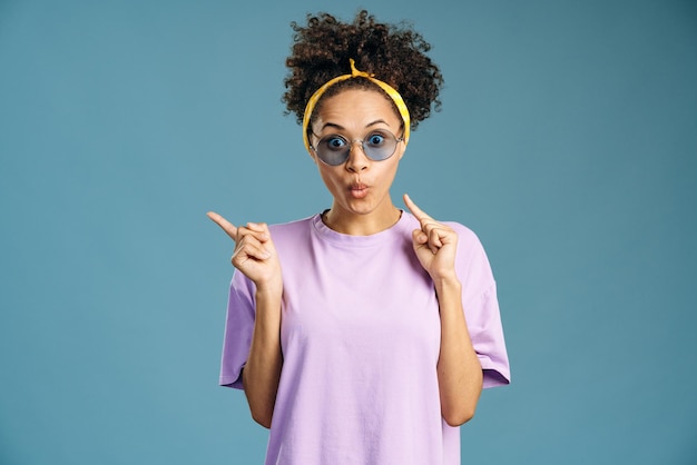 Portrait d'une femme multiraciale étonnée portant des lunettes pointant vers un endroit vide sur fond