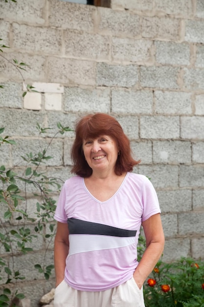 Portrait de femme mûre avec les bras croisés sur la poitrine le jour d'été près du mur gris