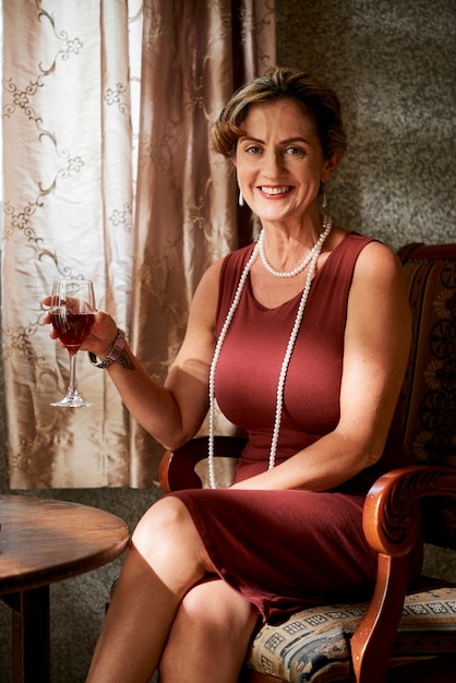 Portrait d'une femme mûre élégante et heureuse avec un collier de perles appréciant un verre de vin rouge