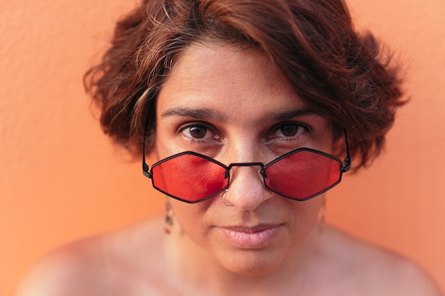 Portrait de femme mûre avec des lunettes de soleil sur fond orange.