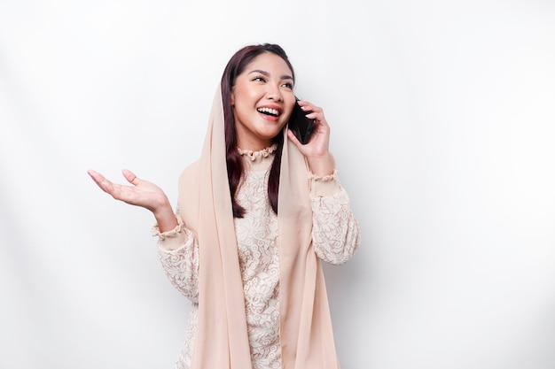 Un portrait d'une femme musulmane asiatique heureuse portant un foulard tenant son téléphone isolé par fond blanc